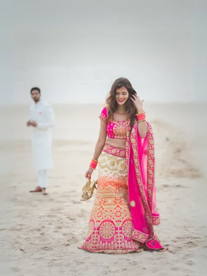 A candid moment on the sand, where the bride, holding her shoes, shares a smile, creating a relaxed and authentic pre-wedding memory.