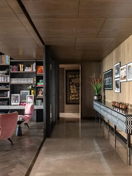 The corridor in the Caitriona apartment, where the flooring transitions from marble to a herringbone wood pattern. A striking 'Missoni Console' with mother-of-pearl inlay stands against a wall of family photos, blending personal touches with high design.