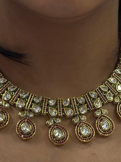 A close-up of a kundan necklace with teardrop-shaped pendants, featuring fine ruby-colored stone work.