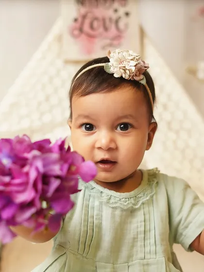 A curious baby offers a flower to the camera. These interactive moments are what make sitter sessions so special and fun.