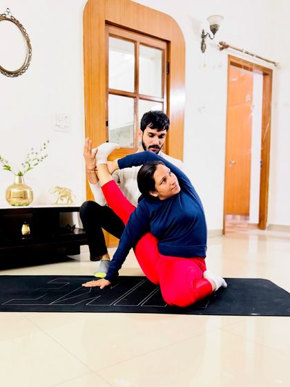 Helping a student with a seated spinal twist and leg extension, focusing on both flexibility and balance.