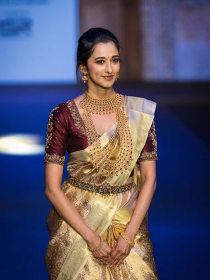 Actress Radhika Narayan gracing the runway in a stunning golden saree. This shot captures her elegant pose, showcasing the traditional jewelry and the richness of the garment for the brand.