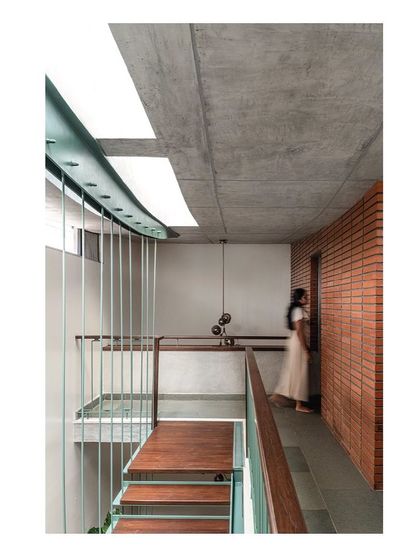 A corridor on the upper floor is defined by an exposed brick wall on one side and a view down into the double-height volume on the other. A linear skylight and slender steel rods acting as a balustrade keep the space feeling light and open.