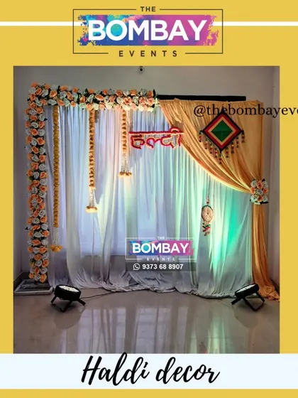 Here is another style for a Haldi ceremony at home. This setup features a beautiful backdrop of yellow and white drapes, a floral border, hanging marigold strings, and a custom floral "Haldi" sign, all lit perfectly for photos.