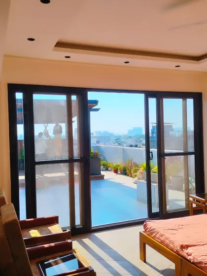 A view from inside a terrace bedroom in Palam Vihar, Gurgaon, looking out onto the newly designed rooftop garden. The large sliding doors connect the indoor and outdoor living spaces.