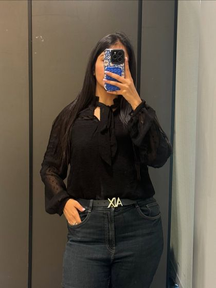 A classic black-on-black look with a tie-neck blouse and dark jeans. This is a timeless and sophisticated outfit that works for any office environment.