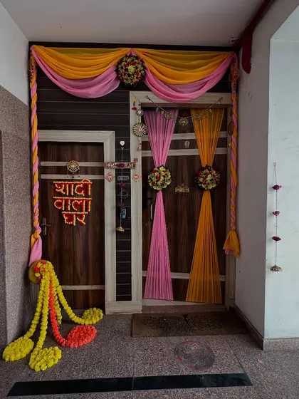 A 'Shaadi Wala Ghar' decoration for an apartment door, using colorful drapes and flower tassels.