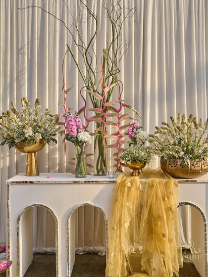 A beautiful console table styled with an artistic arrangement of heliconia and tuberoses in gold and glass vases, draped with a delicate gold fabric.