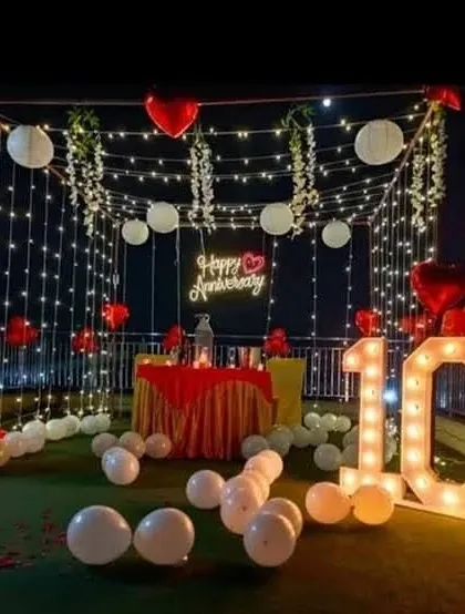 A romantic 10th-anniversary terrace setup with a canopy of fairy lights, red and white balloons, and '10' marquee numbers.