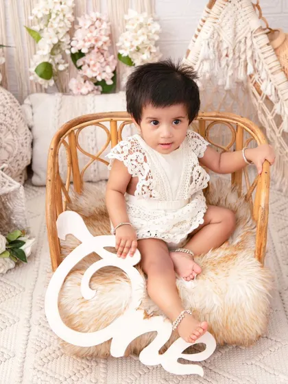 A one-year-old holding a wooden 'One' sign. This is a classic pose for a rustic-themed first birthday shoot.
