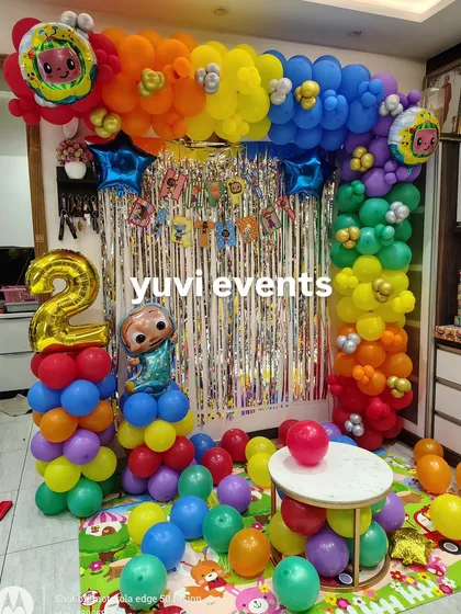 A very colorful Cocomelon-themed setup for a second birthday, with a rainbow balloon arch and character foil balloons.