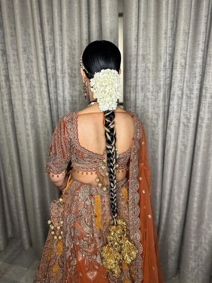 A traditional bridal braid adorned with a large white floral arrangement and a heavy golden parandi.