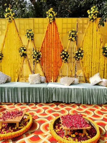 A unique Haldi seating area with a backdrop made of marigold strings arranged in geometric patterns. The low seating and flower-filled urlis complete the traditional look.