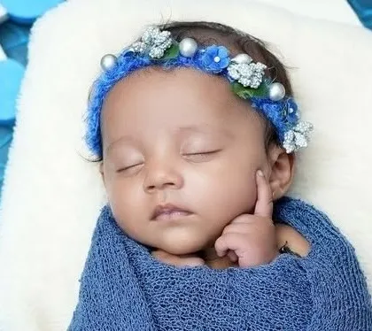 A close-up of a sleeping newborn, swaddled in blue. The focus is on their perfect, peaceful face and tiny hand.