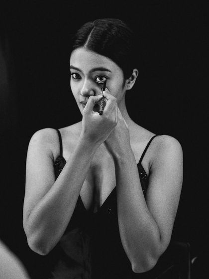 A wider shot of the eyeliner application, showing more of the model's pose. The deep blacks and bright highlights of the monochrome image create a classic, dramatic look.