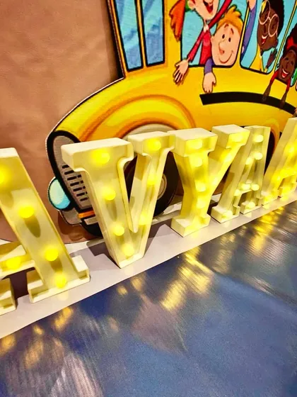 Light-up marquee letters spelling "AVYAAN" in front of a fun school bus cutout.