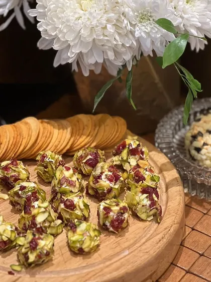 A cheese and cracker board featuring our cranberry and pistachio cheese bites alongside a block of herb-crusted cheese, ready for guests to enjoy.