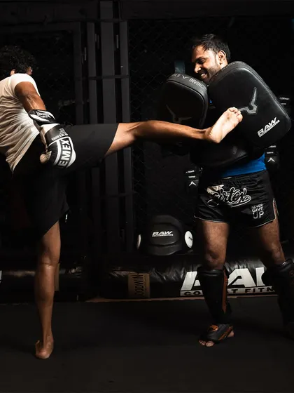 A fighter connects with a side kick on a coach's pads, showing the dynamic nature of our training.