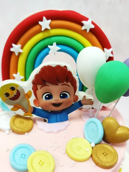 A close-up of our Cocomelon cake, featuring JJ and a baby shark friend set against a vibrant rainbow and colorful button details.