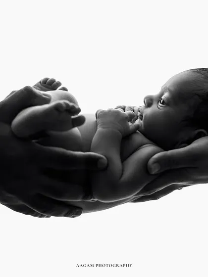 A minimalist and artistic newborn portrait. The baby, held in parental hands against a white background, appears as a precious gift, the center of their world.