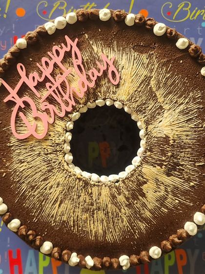 A bundt-style chocolate cake with a rich ganache, dusted with cocoa powder and decorated with simple buttercream dots. The shape makes it a little different from a standard round cake.