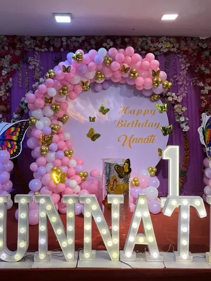 I specialize in creating magical first birthday parties, like this butterfly theme for Unnati. The setup includes a custom circular backdrop, a full balloon arch in pink and gold, and large light-up marquee letters spelling out the name for a perfect photo opportunity.