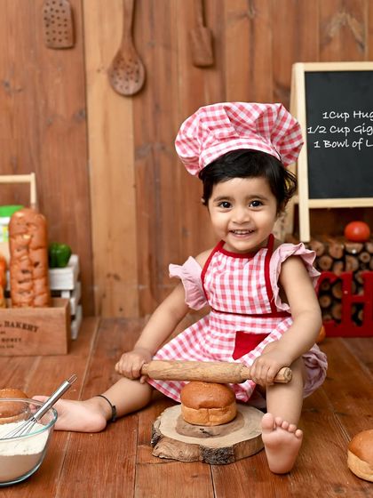 The cutest little chef in the kitchen! Dressed in a gingham apron and chef's hat, this baby is ready to roll some dough and bake up some smiles for her first birthday.