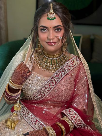 A close-up of the bride's face, framed by her beautiful updo and delicate nath. The hairstyle is designed to balance the entire look.