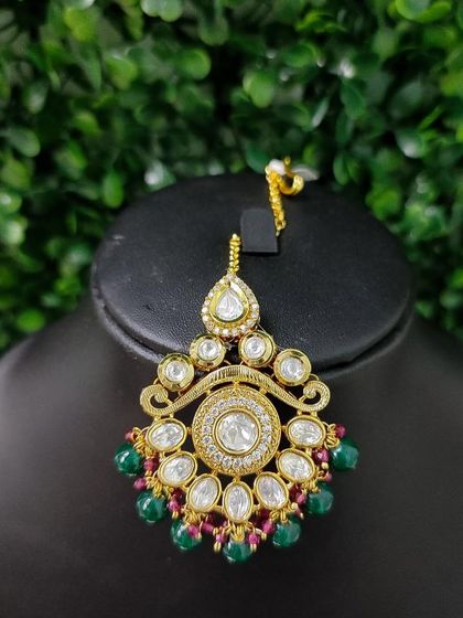 A classic kundan maang tikka with a circular design, accented with green and red beads.
