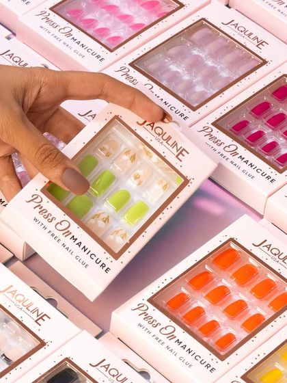 A top-down shot of a hand picking a box of press-on nails from a large, colorful selection. This showcases the variety of designs available.