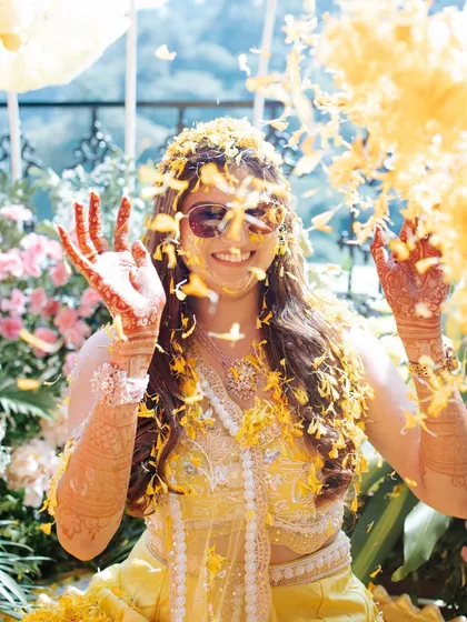 A bride enjoying a shower of marigold petals during her Haldi. Her carefree smile and the vibrant yellow flowers create an image of pure happiness. This is what a celebration of love looks like.