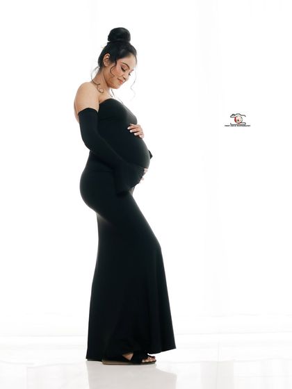 A graceful side-profile shot of the mother-to-be in a form-fitting black gown. Her gentle expression as she looks down at her bump conveys a quiet and profound connection.