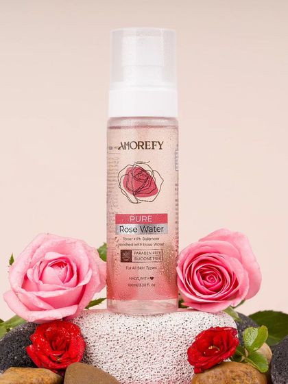 A bottle of pure rose water surrounded by fresh pink roses. This classic styling approach clearly communicates the product's main ingredient and natural fragrance.