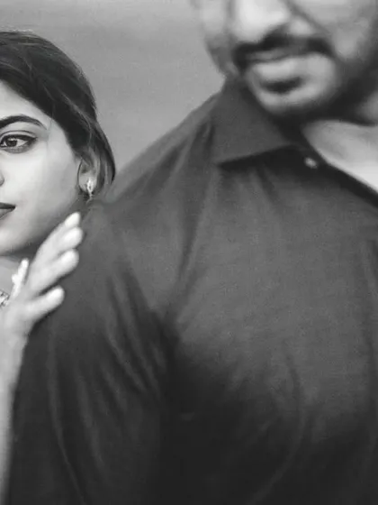 A classic black and white portrait with an artistic feel. The bride looks towards the groom, whose figure is in the foreground, creating a moody and thoughtful composition.