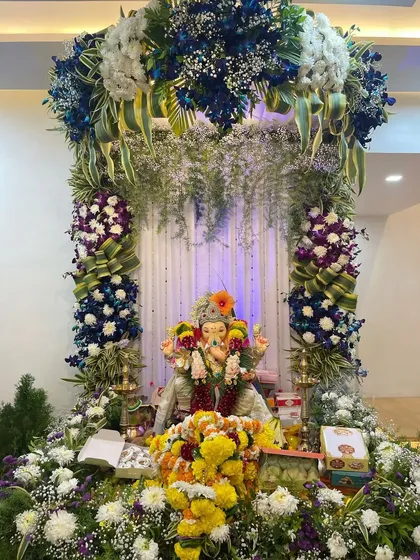This lush Ganpati decoration uses a mix of blue orchids, white hydrangeas, and fresh greenery. The arrangement creates a rich, textured floral arch that looks both natural and grand.