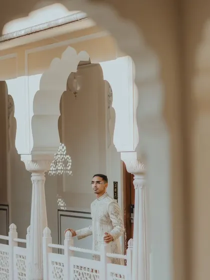 A wide shot of the groom standing in a beautifully arched hallway, creating a sense of grandeur.