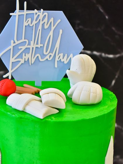 A close-up of the cricket-themed cake, showing the detail on the fondant pads, bat, and ball.
