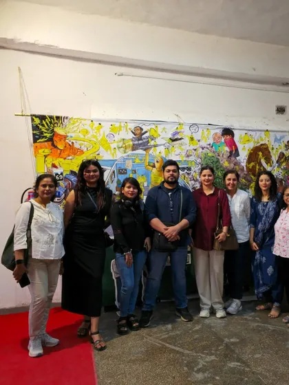Our students and instructors pose together in front of a large, vibrant mural at the College of Art.