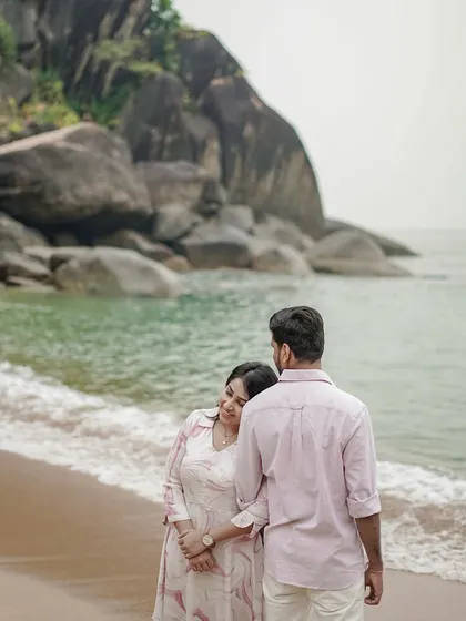 A quiet, tender moment on the beach, with the woman resting her head on her partner's shoulder as they look out at the sea. A beautiful, candid pre-wedding photograph.