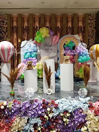 A whimsical stage setup combining hot air balloons, teddy bears, and pampas grass. The decor features a vibrant floral base, pastel balloons, and various props to create a dreamy and gentle atmosphere.