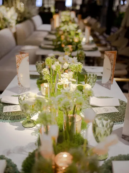 An example of our integrated approach to decor and dining. This elegant table setting features a lush moss runner, delicate white florals, and custom menus, creating a cohesive and enchanting garden-themed dining experience for guests.