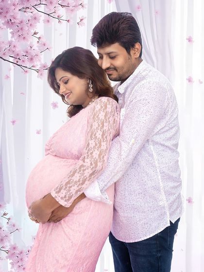 A gentle and romantic pose with the couple surrounded by a soft, dreamy floral background. The mom-to-be's pink lace dress adds to the delicate feel of the portrait.