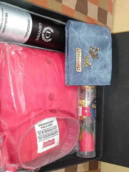 This vibrant gift hamper includes a personalized denim wallet, a bright pink shirt, deodorant, and a decorative rose with chocolates.