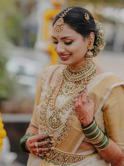 A picture of pure grace. This bride's look is a testament to classic elegance, with her golden Kanjeevaram saree, layered temple jewellery, and a makeup look that is both radiant and understated, letting her natural happiness shine through.