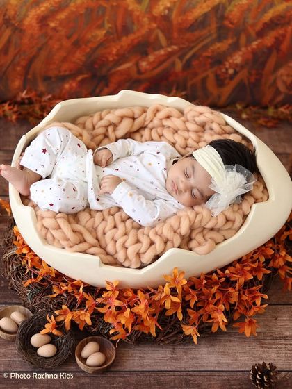 A newborn rests in our eggshell prop, set against an autumn-themed backdrop with orange leaves and a cozy knit blanket.