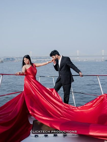 A chivalrous moment on a yacht in Goa, with the groom kissing the bride's hand as her magnificent red gown flows around them.
