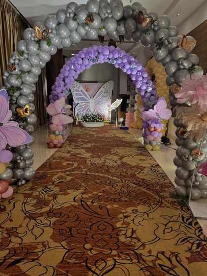 A breathtaking entrance for a butterfly themed party, featuring a long walkway under a tunnel of silver and purple balloon arches.