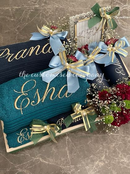 An indulgent hamper designed for couples, featuring personalized bath towels for "Pranav" and "Esha." The set is beautifully arranged on a tray with fresh flowers, creating a luxurious and practical gift.