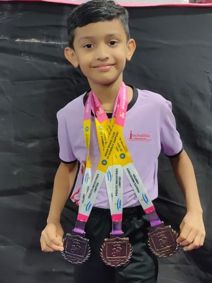 A young champion proudly displays the three medals he won at the Bhausaheb Navodit Gymnastics Competition. His success is a result of his dedication, discipline, and passion for the sport.