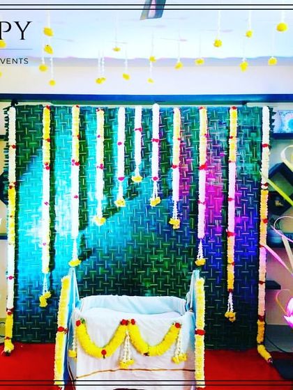 A simple and traditional cradle ceremony decoration for home events. The backdrop is made of woven green mats with hanging tuberose garlands.